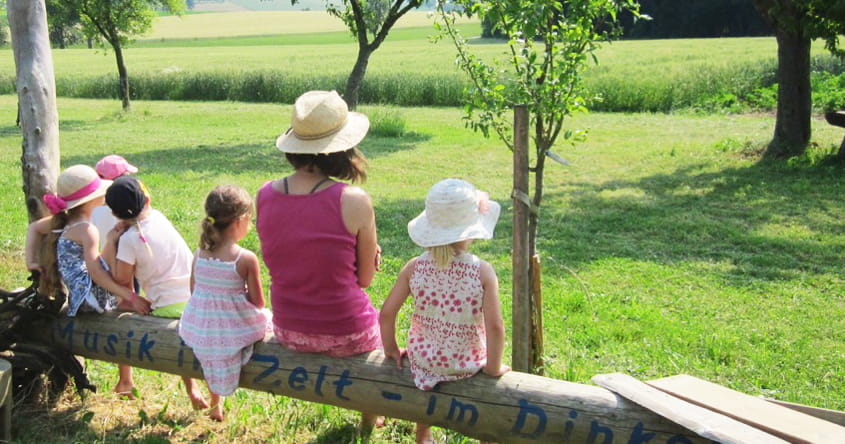 Kinder und Pädagogin sitzen auf einem Baumstamm