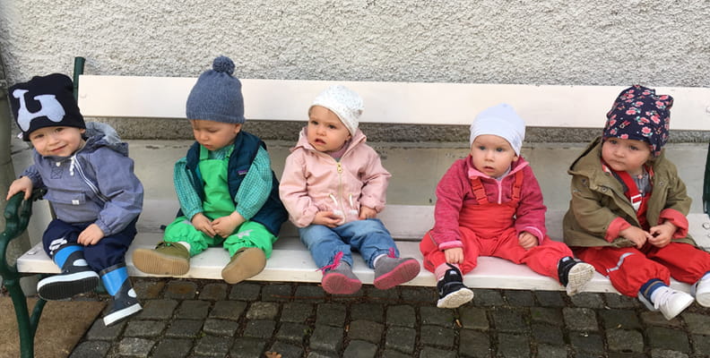 Fünf Kleinkinder sitzen auf einer Parkbank