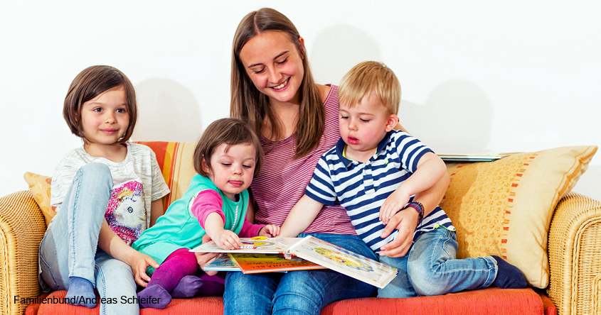 Frau liest drei Kindern auf dem Sofa vor