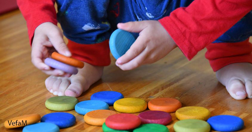 Kinderhände spielend mit bunten Holzplättchen