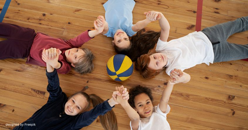 Kinder liegen auf dem Boden in einem Kreis und halten sich an den Händen