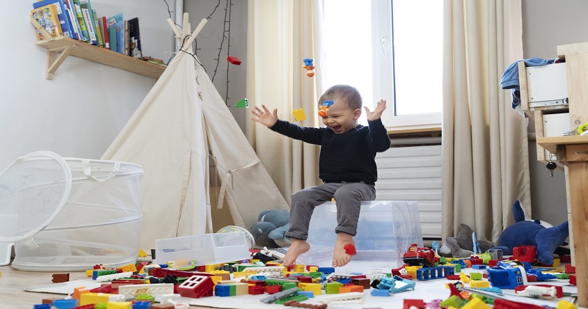 Kind sitzt auf dem Bett auf dem Boden türmt sich das Legochaos