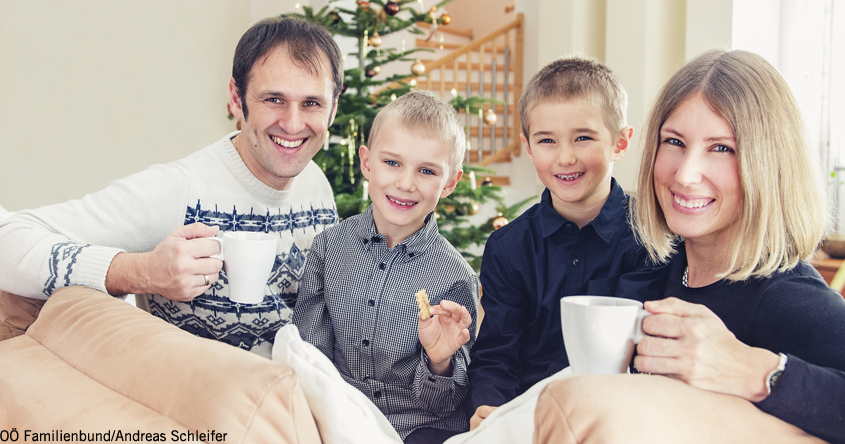 Eine Familie die vor dem Weihnachtsbaum Kakao trinkt.