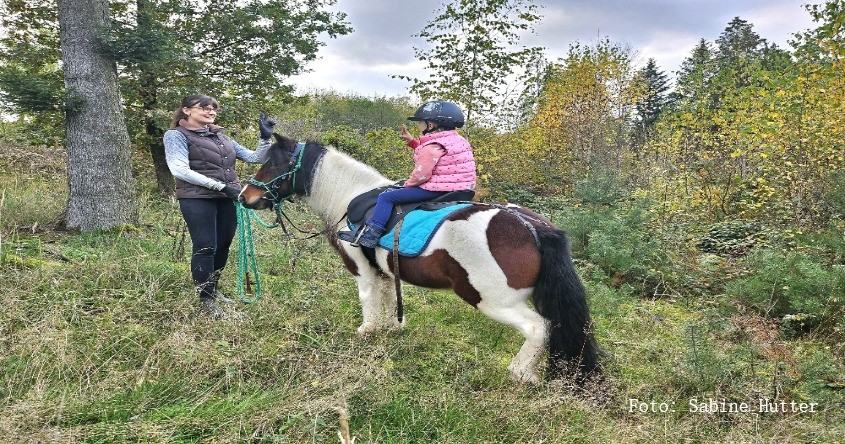 Frau hält Pony mit Kind im Sattel