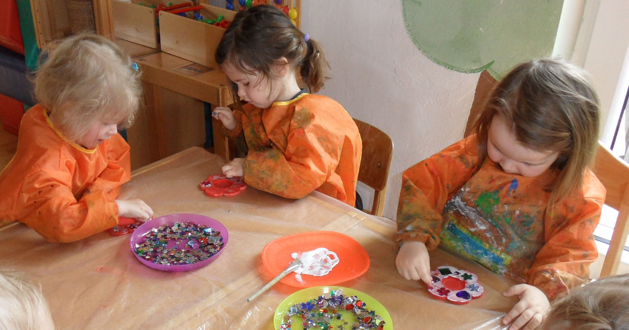 Kinder in Malschürzen sitzen um den Basteltisch