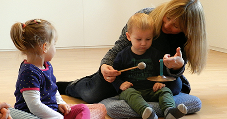 eine Frau mit einem Becken in den Händen und 2 Kinder sitzen am Boden