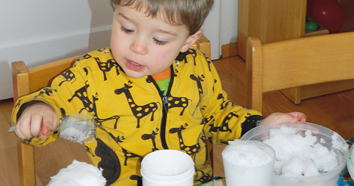 kleiner Junge der mit Schnee gefüllten Bechern spielt