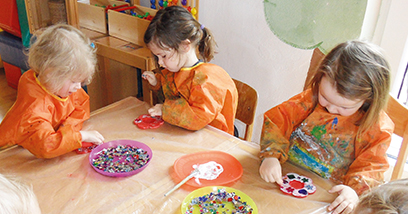 Kinder in Malschürzen sitzen um den Basteltisch