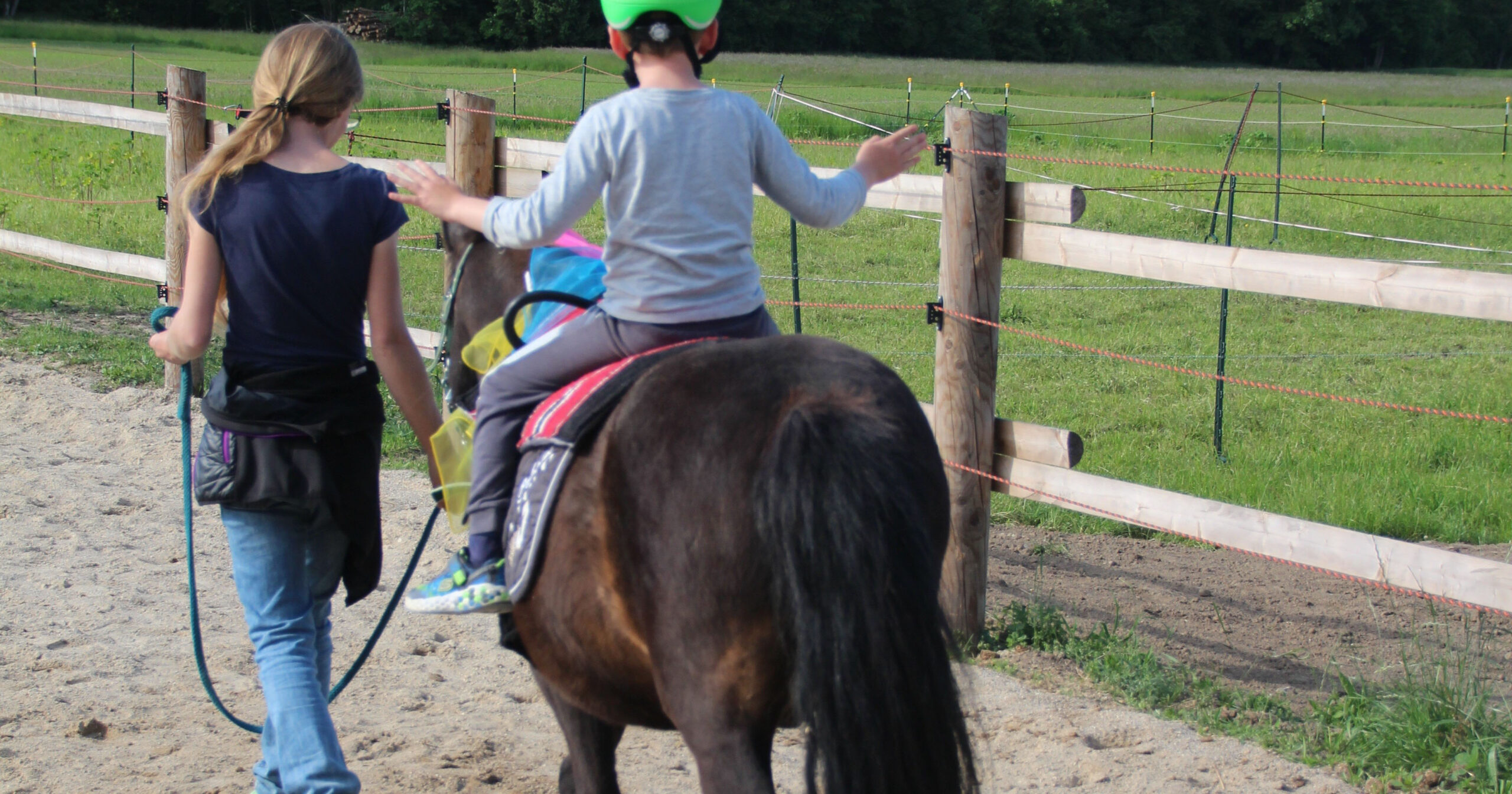ein Kinde sitzt am Pony das am Zügel geführt wird vom Erwachsenen